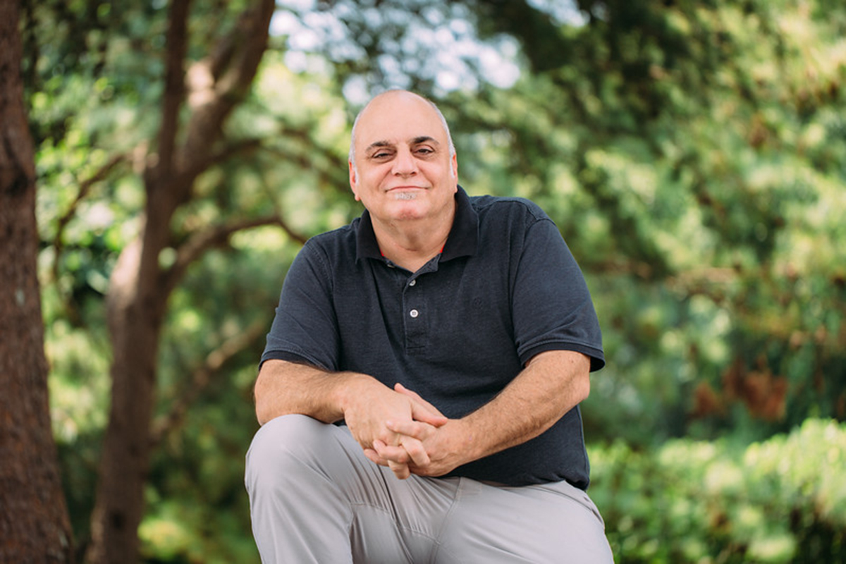 Outdoor, environmental portrait of Stuart Turner, smiling, with forearms resting on one knee.