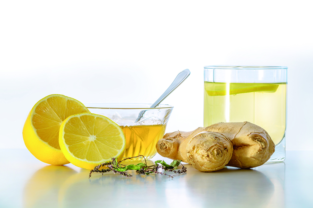 Studio art of lemons, and ginger, together with a glass of water and spoon.