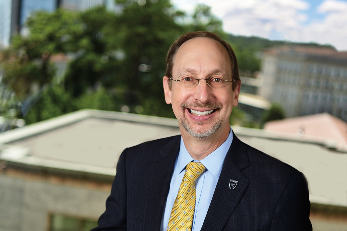 Portrait of Jonathan Lewin in a coat and tie, with Emory University buildings in the background.