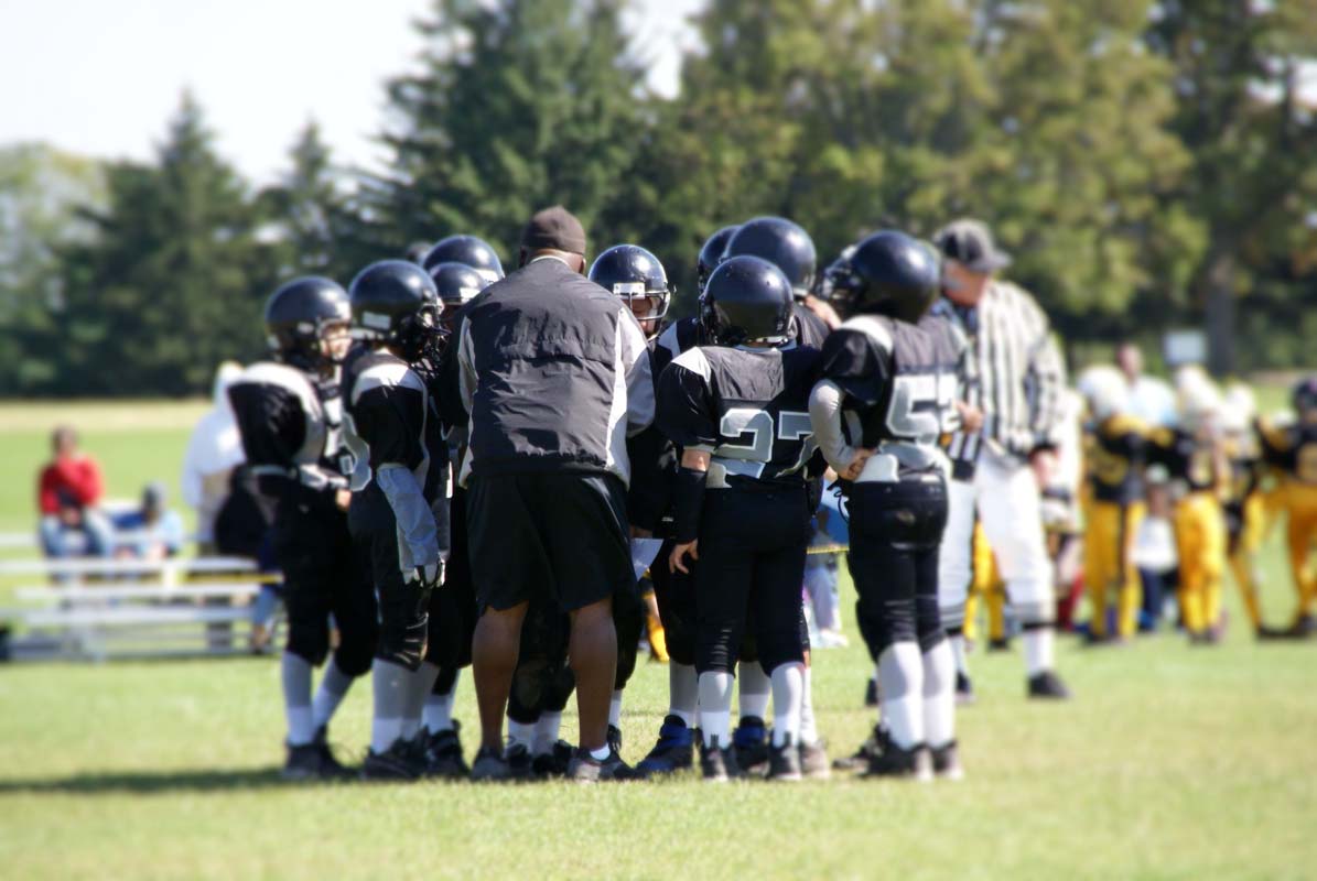 a pee-wee league football teams huddles around its coach