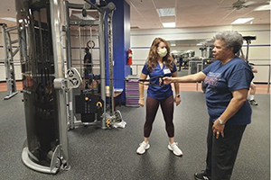 A trainer works with a woman in the wellness center exercise room
