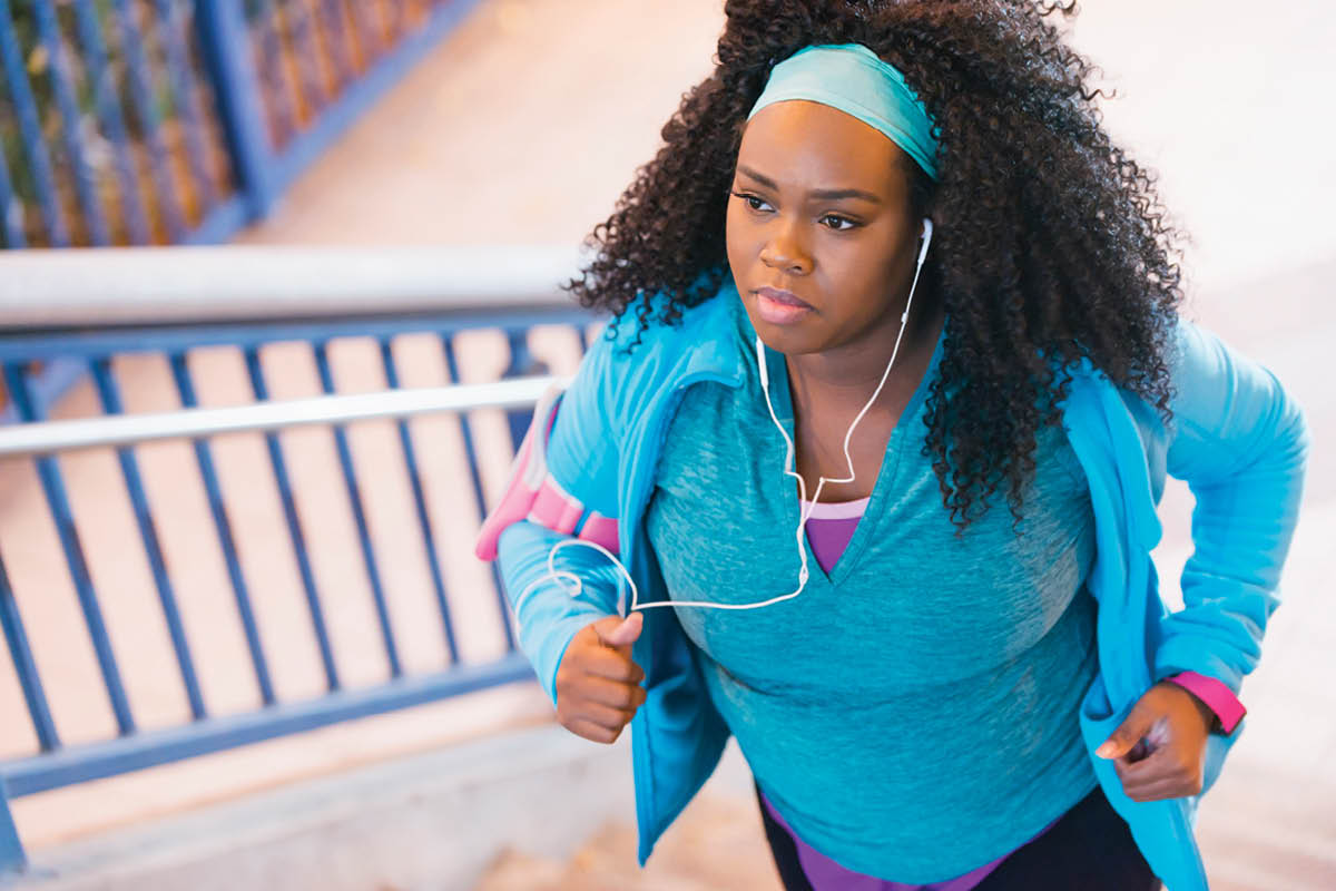 Photo of woman jogging up the stairs in an all blue outfit with headphones on